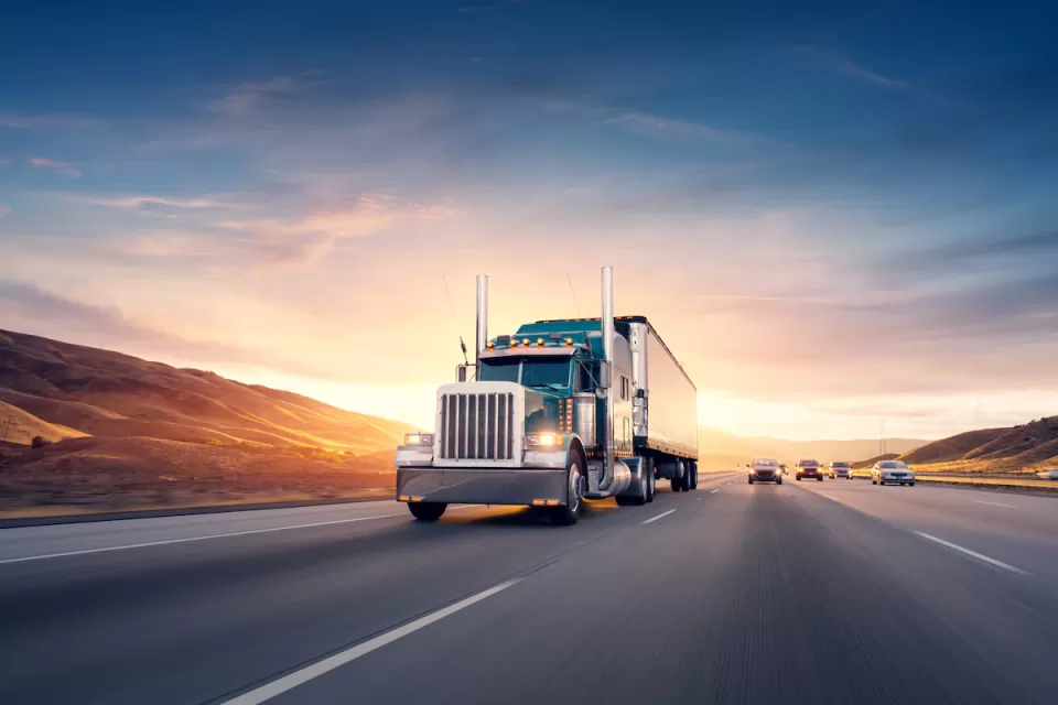 Semi truck driving down freeway with twilight sky in background.